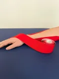 Ein getapter Arm liegt auf einer Behandlungsbank und ist mit einer Taperolle umwickelt